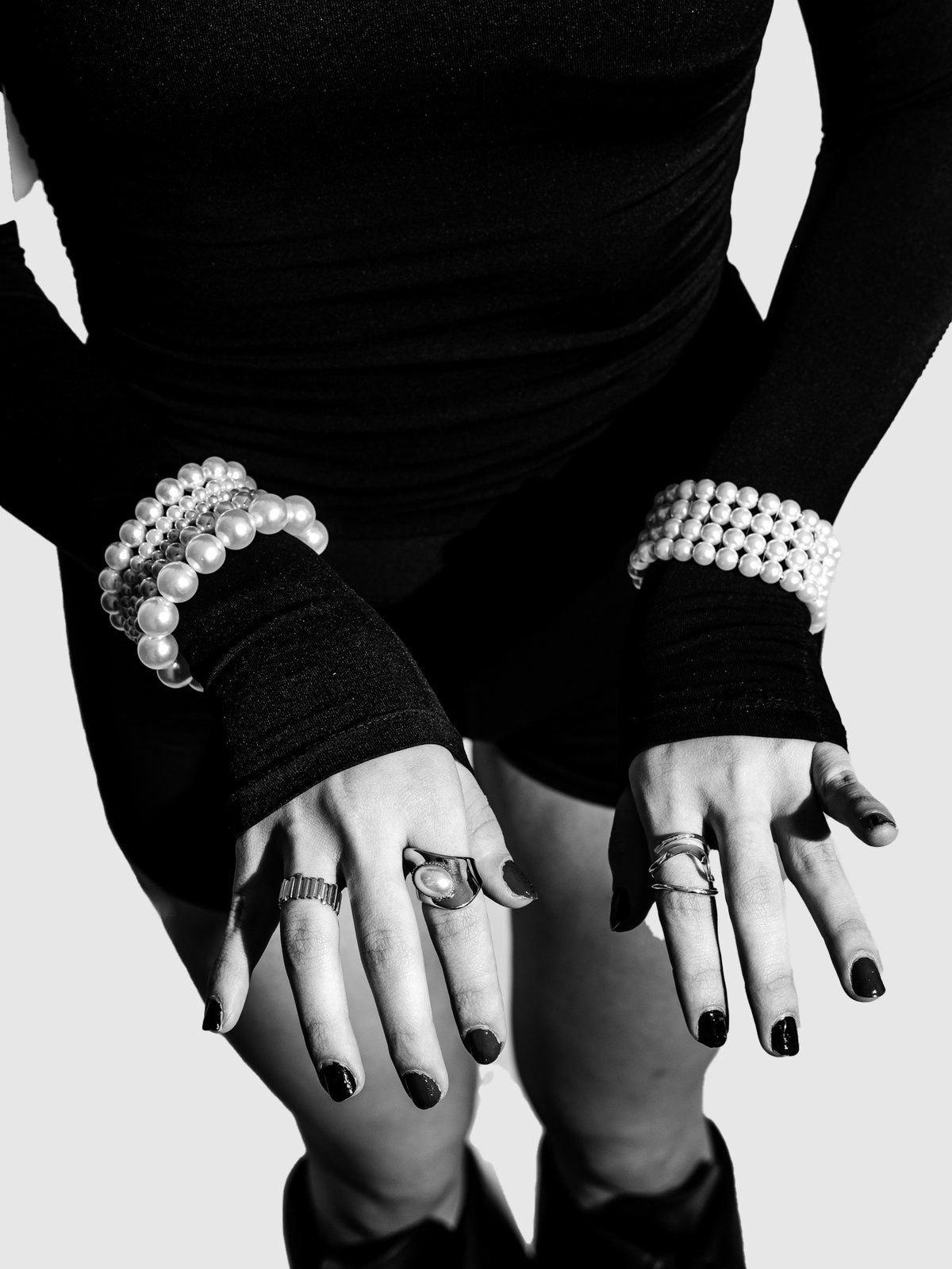 Pearl bracelets on both wrists, hands on the knees