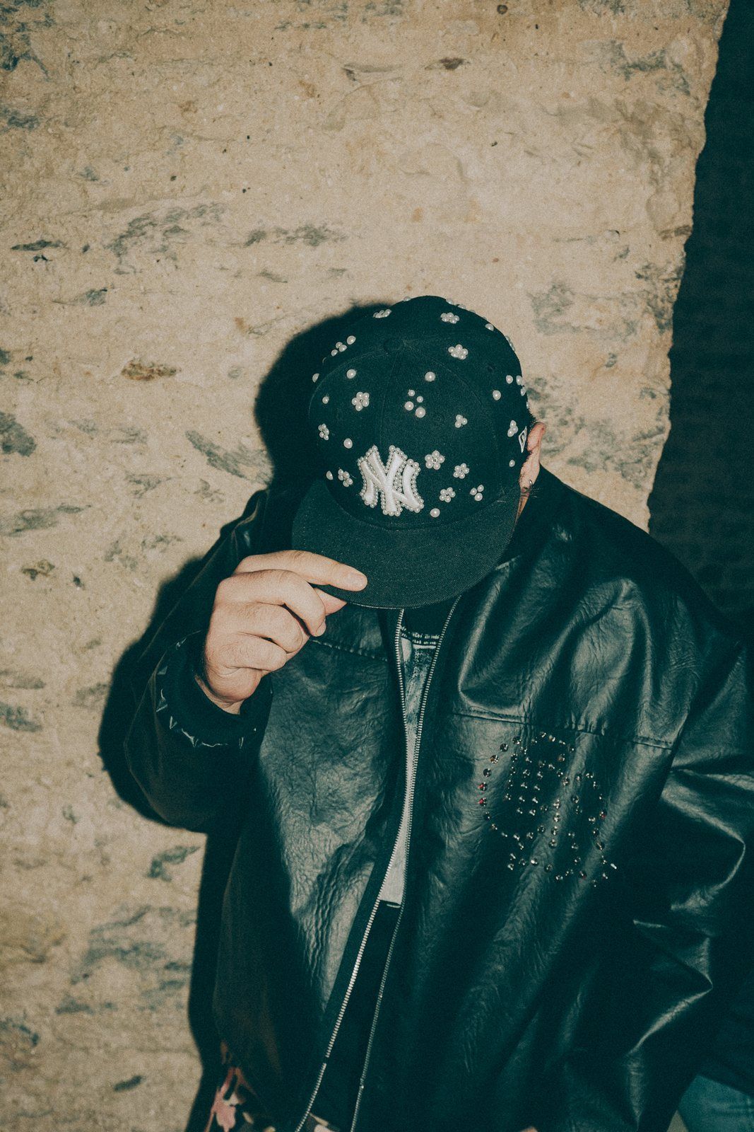 Pearl black cap held against a stone wall