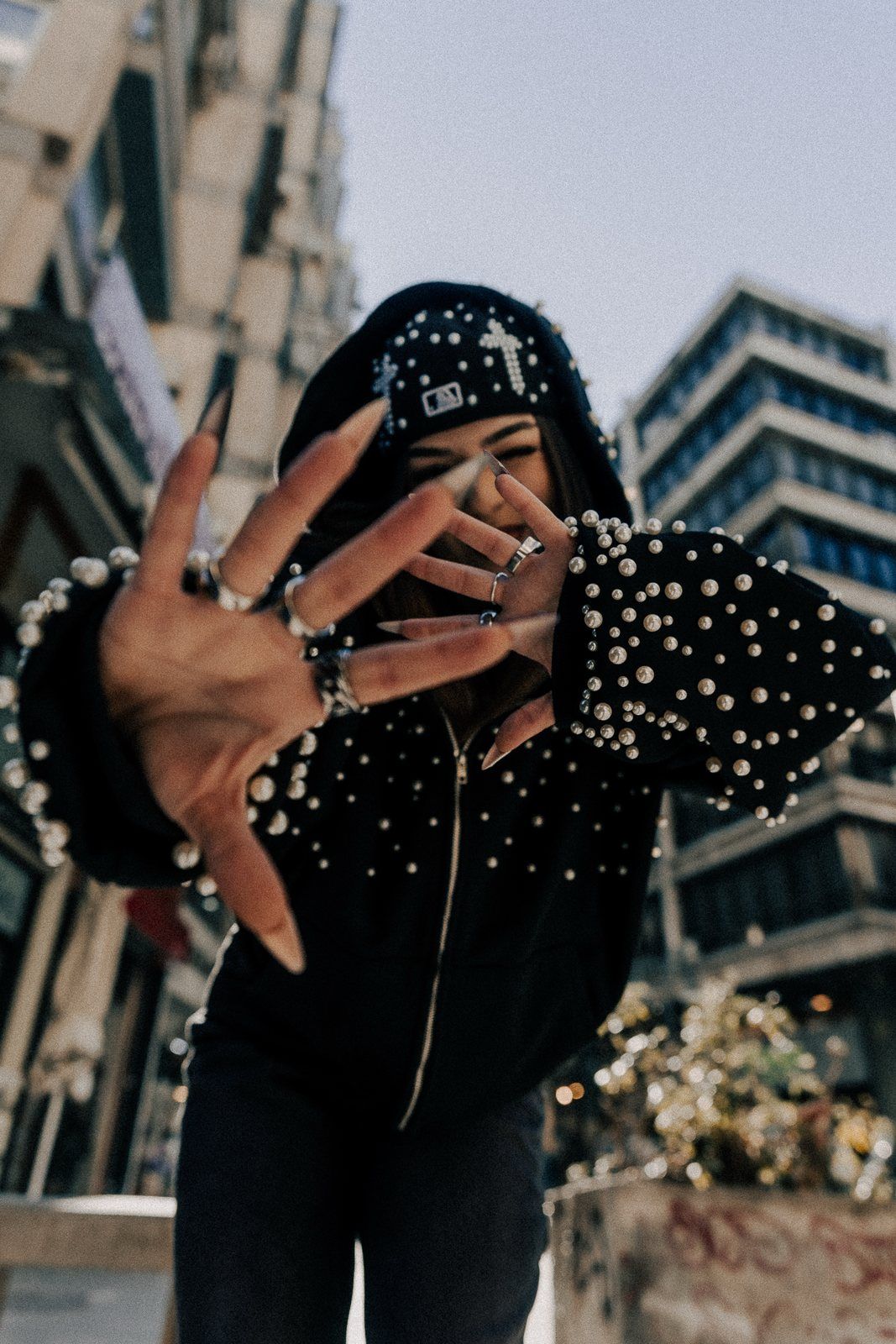 Pearl zip-up on a city street, hand spread toward the camera